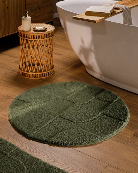 Runder Badevorleger mit strukturiertem Muster in hellem Badezimmer mit freistehender Badewanne, Rattanbeistelltisch und Holzboden.