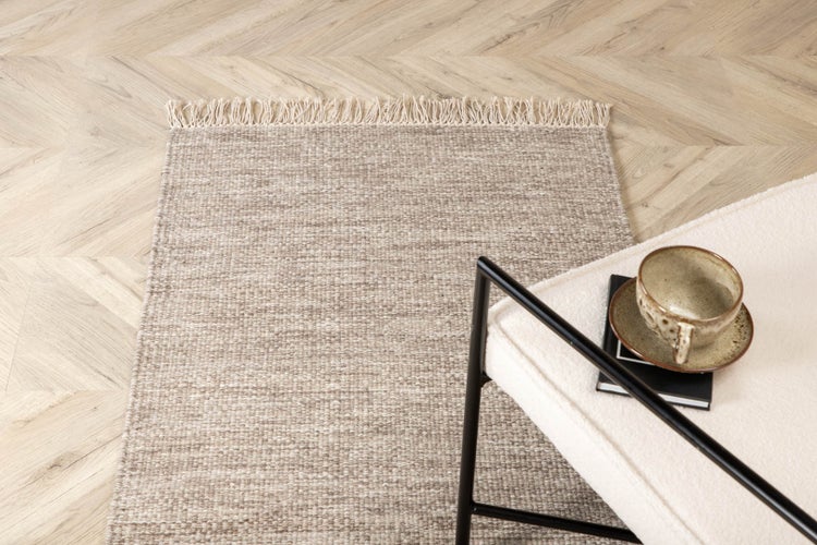 Beiger Teppich mit Fransen neben einem Stuhl mit Buch und Tasse