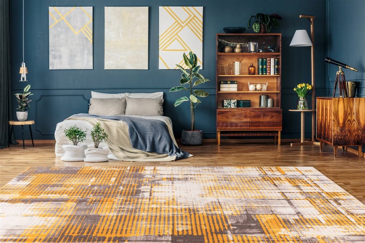 Moderner Teppich mit abstraktem Muster in Gelb und Grau auf Holzboden in einem Schlafzimmer mit dunkelblauer Wand und Holzmöbeln.