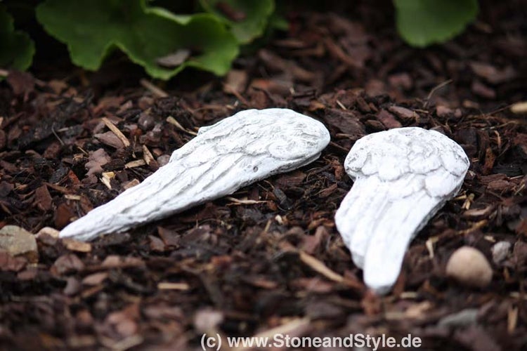 Zwei dekorative Engelsflügel aus Steinguss zur Gartendekoration auf Rindenmulch platziert.