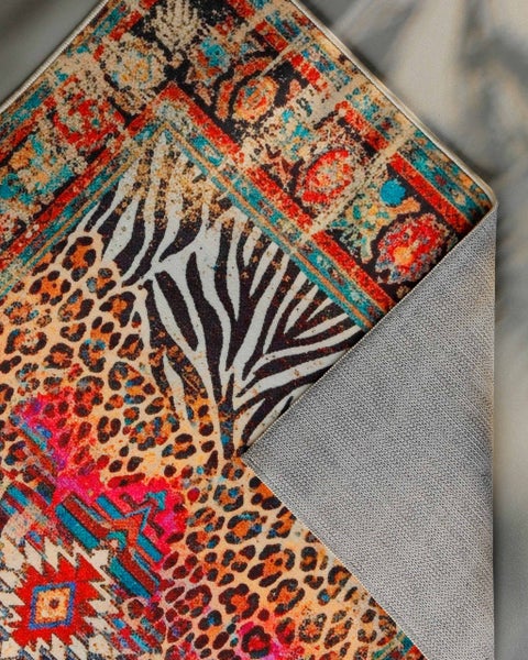 Bunter Teppich mit Leoparden-, Zebramuster und orientalischen Motiven. Umgeschlagene Ecke zeigt graue, rutschfeste Unterseite.