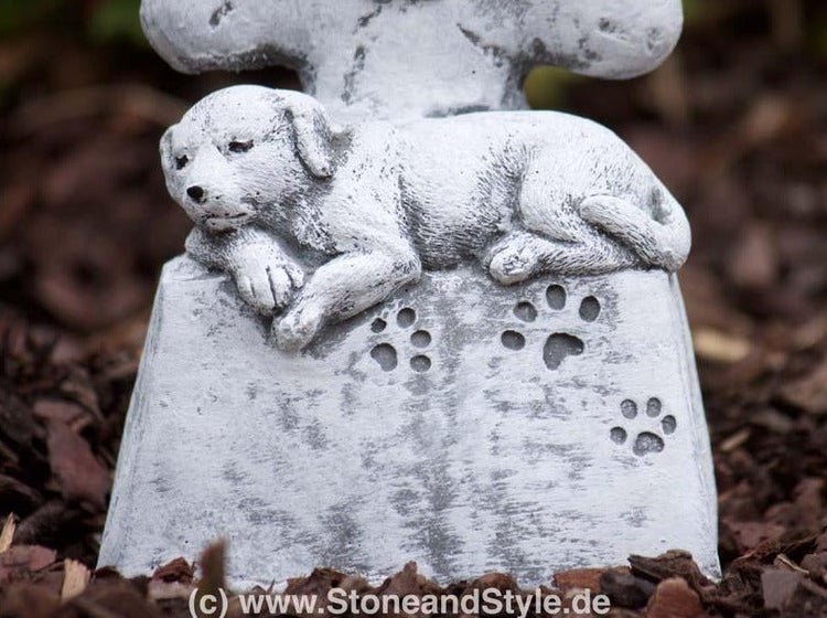 Gartendekoration Grabstein für Haustiere aus Stein mit liegendem Hund und Pfotenabdrücken als Gedenkstein für den Garten.