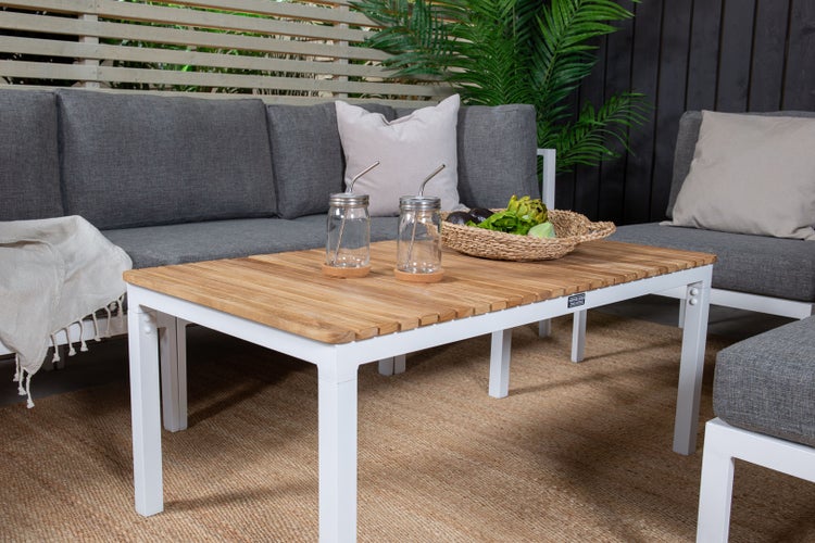 Gartenszene mit einem Tisch, zwei Gläsern mit Strohhalmen, einer Schale mit Gemüse und einem grauen Sofa mit Kissen