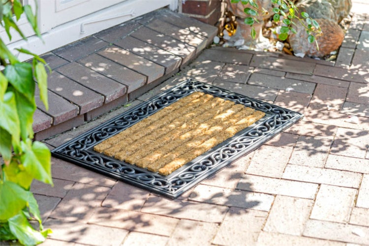 Fußmatte aus Kokos mit dekorativem Rahmen vor einer Haustür