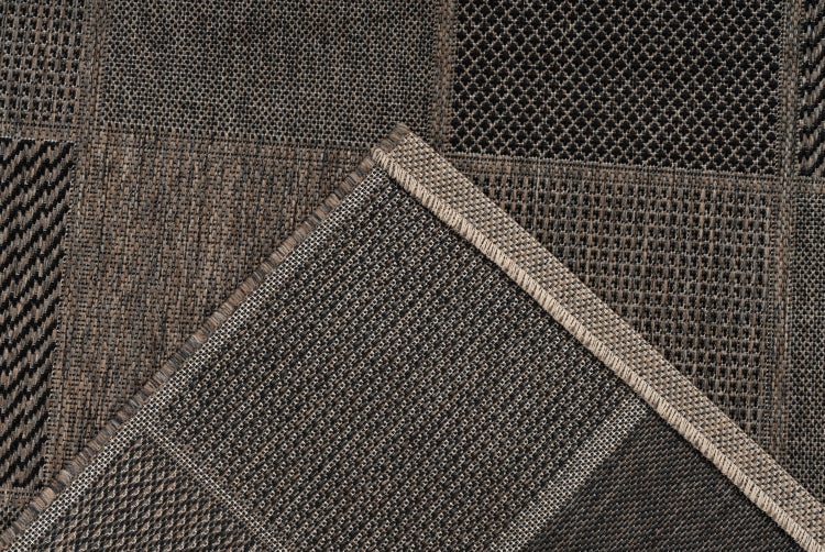 Detail eines flachgewebten Teppichs mit Patchworkmuster in Braun und Grau, umgeschlagene Ecke mit Randkettelung.