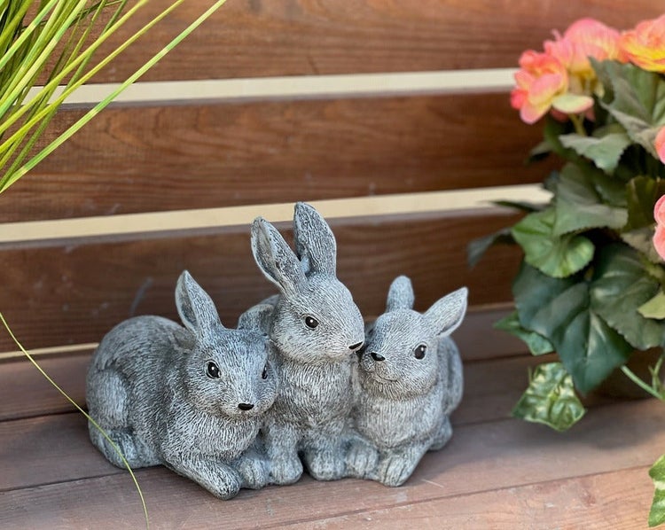 Drei sitzende Hasen Dekofiguren aus Kunststein als Garten Deko auf einem Holztisch.