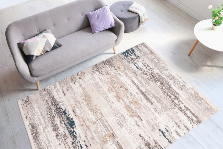 Teppich mit abstraktem Muster vor grauem Sofa in hellem Wohnzimmer mit Laminatboden.