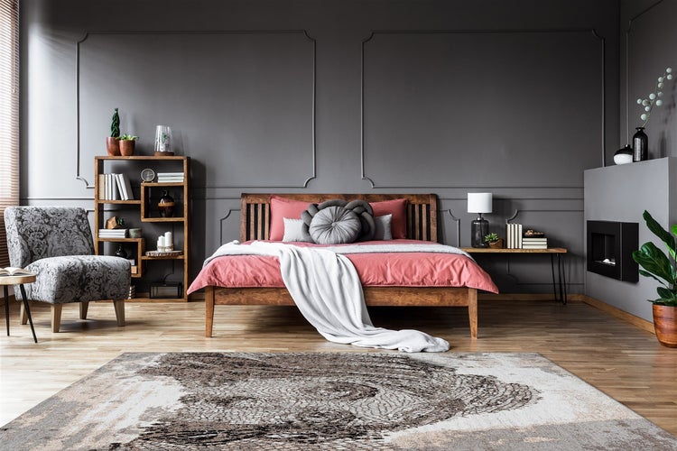 Modernes Schlafzimmer mit Holzbett, dunklen Wandpaneelen, gemustertem Sessel und großem Teppich auf hellem Holzboden.