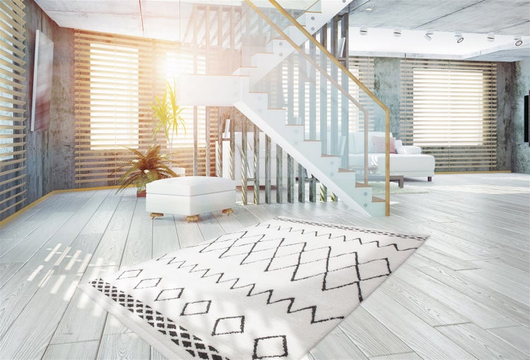 Moderner Teppich mit geometrischem Muster in einem hellen Wohnzimmer mit weißem Holzboden, Treppe und Jalousien.