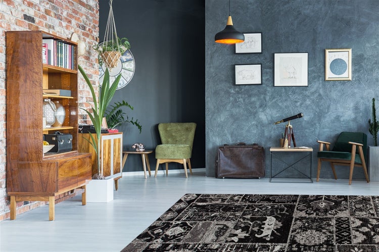 Patchwork-Teppich in einem Wohnzimmer mit Ziegelwand, blau strukturierter Wand, Vintage-Holzmöbeln und grünen Sesseln.