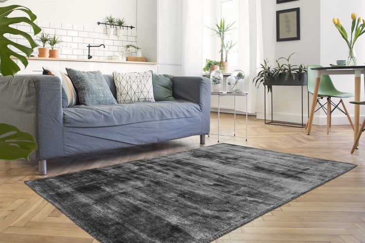 Dunkelgrauer strukturierter Teppich in einem hellen modernen Wohnzimmer mit grauem Sofa, Parkettboden und Zimmerpflanzen.