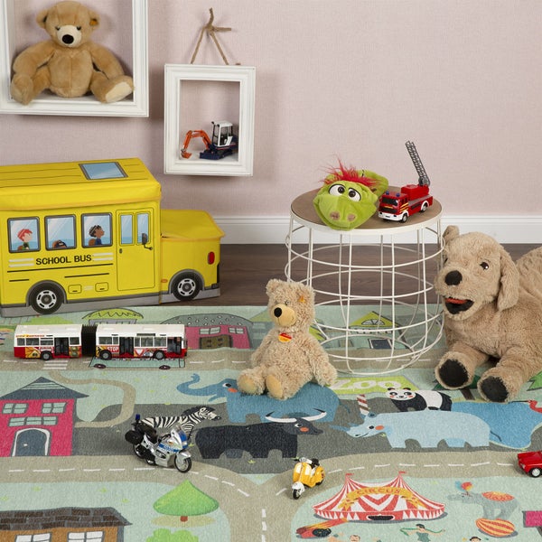 Hell gestaltetes Kinderzimmer mit einem bunten Spielteppich mit Zoo- und Stadtmotiven, Spielzeugautos, Stofftieren und einer gelben Spielzeugkiste.
