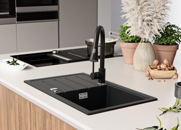 Schwarzes Spülbecken mit Abtropffläche und Armatur in einer hellen Küche.