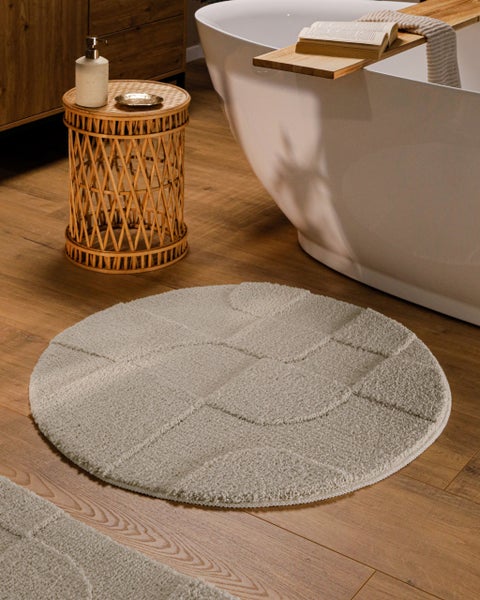 Runder Badteppich mit strukturiertem Muster in einem modernen Badezimmer neben einer freistehenden Badewanne und einem Rattan-Beistelltisch.