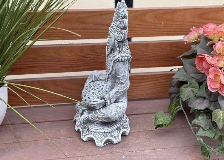 Gartenfigur aus grauem Steinguss, sitzende asiatische Gottheit mit verzierten Kopfschmuck und dekorativer Kugel.