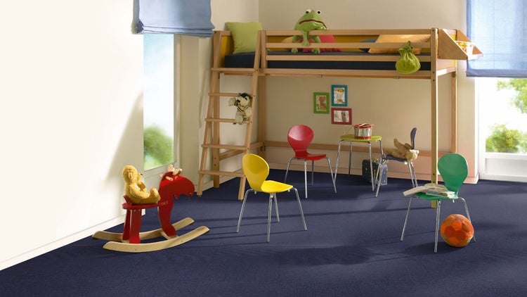 Helles Kinderzimmer mit Hochbett, bunten Möbeln und dunkelblauen Teppichfliesen in Schachbrett-Optik.