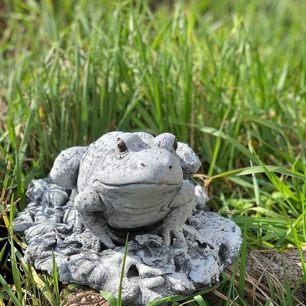 Steinfigur eines Frosches auf einem Blattsockel zur Gartendekoration im Gras