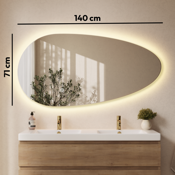 Organisch geformter LED Badspiegel mit 140 mal 71 Zentimeter, wandmontiert über einem Doppelwaschtisch mit Holzunterschrank und goldenen Armaturen.