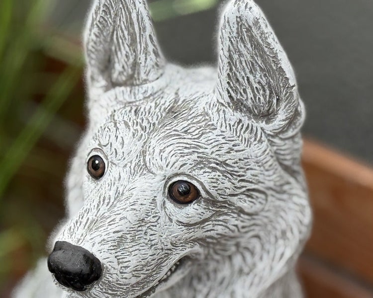Nahaufnahme einer Gartenfigur in Form eines Hundekopfes aus Steinguss mit detaillierter Fellstruktur und braunen Augen.