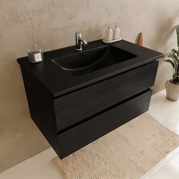 Moderner Waschtischunterschrank mit zwei Auszügen und integriertem Waschbecken in dunkler Optik vor einer strukturierten Wand im Badezimmer.