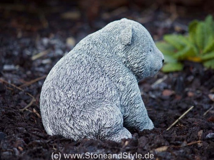 Dekorative Gartenfigur in Form eines sitzenden kleinen Bären aus Stein als Blickfang für das Blumenbeet.