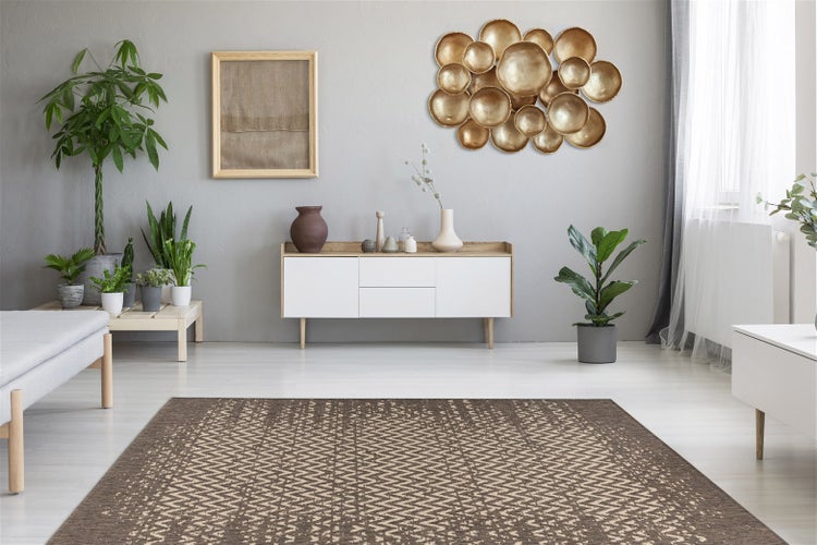 Moderner Wohnraum mit einem großflächigen Teppich mit braun-beigem Zickzackmuster auf hellem Boden vor einem Sideboard und Zimmerpflanzen.