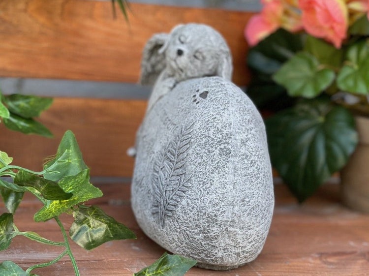 Gartenfigur Hund aus Steinoptik mit Farnblatt Relief auf einem Stein liegend zur Dekoration im Außenbereich