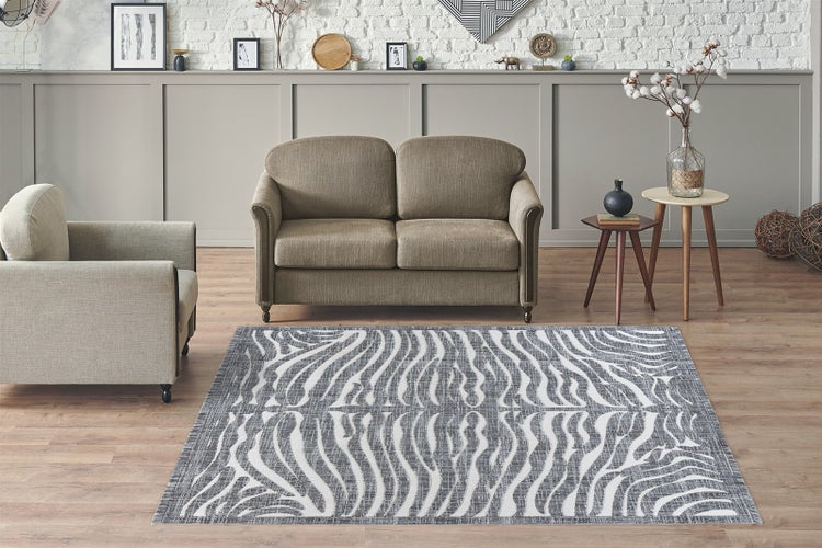 Moderner Wohnraum mit gemustertem Teppich im Zebra-Design vor einem Sofa und Sessel auf Holzboden.