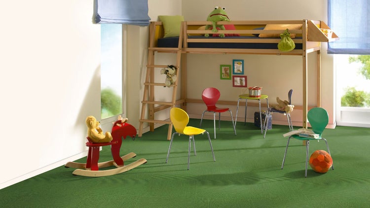 Grüner Teppichboden in einem hellen Kinderzimmer mit Hochbett, bunten Stühlen und einem Schaukelpferd.