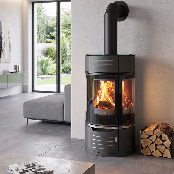 Moderner Kaminofen mit Sichtfenster und brennendem Feuer in einem hellen Wohnzimmer mit Kaminholzstapel.