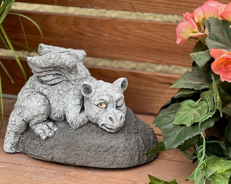 Gartenfigur eines liegenden Drachen auf einem Stein, dekorative Figur in Steinoptik für den Außenbereich.