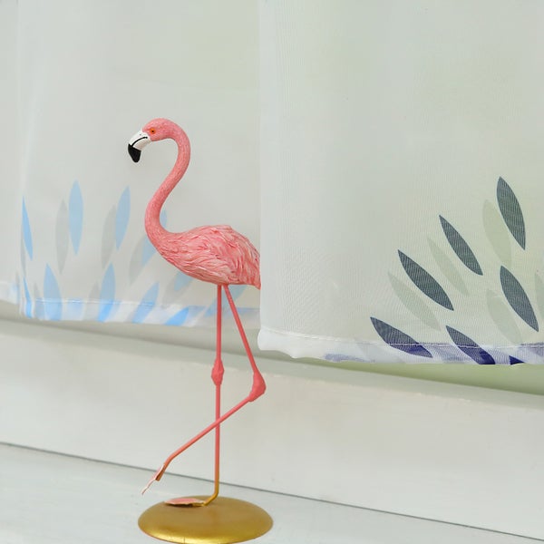 Dekofigur Flamingo vor einer Gardine mit Blätter-Motiv
