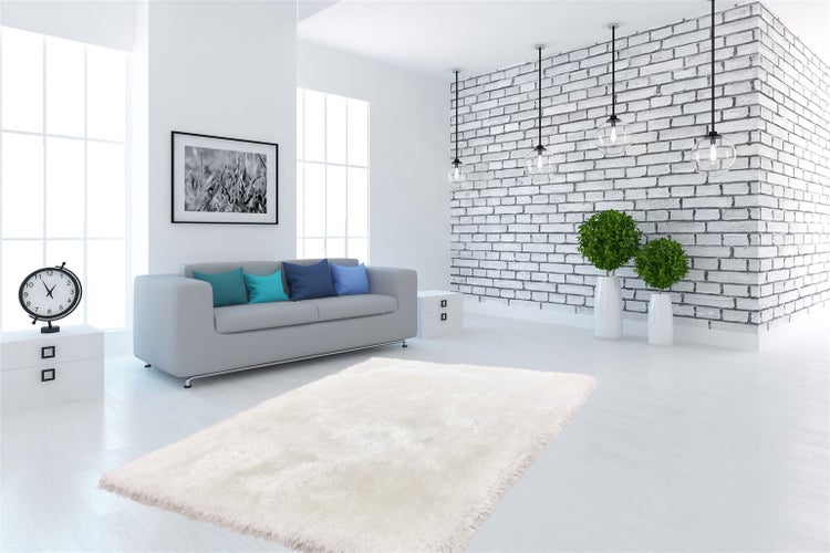 Helles Wohnzimmer mit weißem Hochflor-Teppich, grauem Sofa, weißer Ziegelwand und großen Fenstern. Modernes Design.