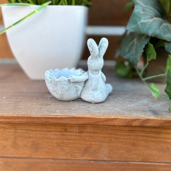 Osterdekoration aus Beton in Form eines sitzenden Osterhasen mit einer Eierschale als Pflanzgefäß oder Schale für Dekoration.