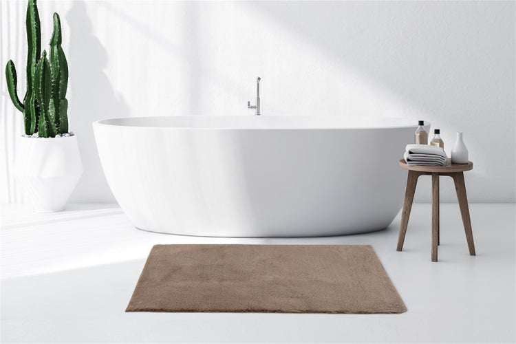 Rechteckige, flauschige braune Badematte vor einer freistehenden weißen Badewanne in einem hellen, minimalistischen Badezimmer.