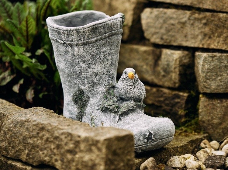 Pflanzgefäß in Stiefelform aus Stein mit einer kleinen Vogel-Figur als Gartendekoration.
