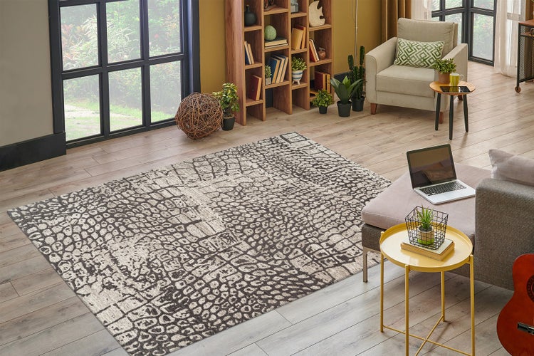 Heller, moderner Wohnraum mit gemustertem Teppich auf Holzboden, Bücherregal und großer Fensterfront.