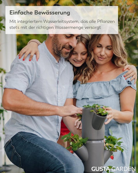 Familie gärtnert gemeinsam im Freien mit einem vertikalen Gusta Garden Erdbeerturm mit integriertem Bewässerungssystem. Gusta Garden Logo.