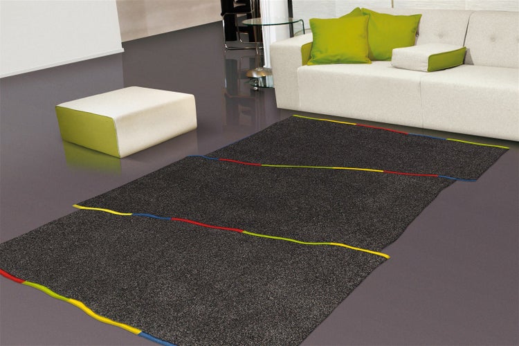 Moderner dunkelgrauer Teppich mit bunten Wellenlinien in einem hellen Wohnzimmer vor einem hellen Sofa mit grünen Kissen.