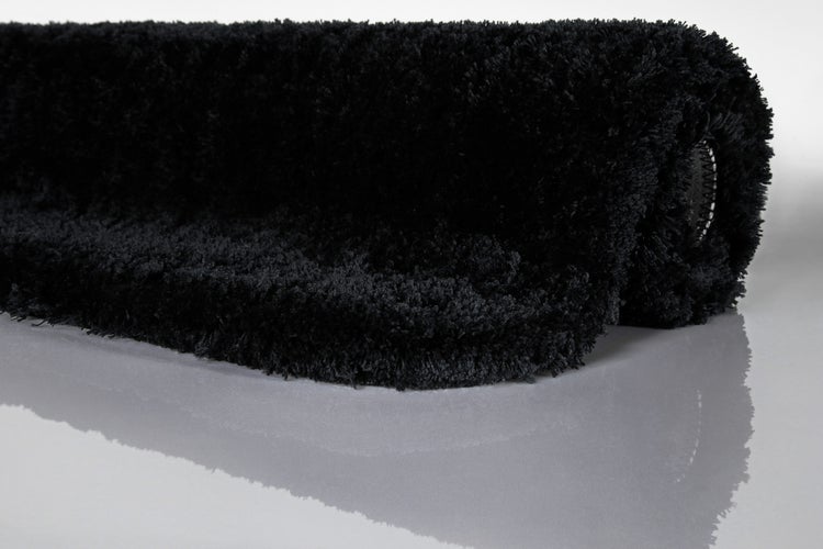 Schwarze Hochflor-Badematte aus weichem Material, zusammengerollt.