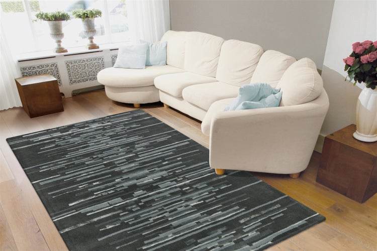 Moderner Wohnraum mit hellem Holzboden, cremefarbenem Sofa und einem rechteckigen Teppich mit abstraktem Streifenmuster in Grau und Weiß.