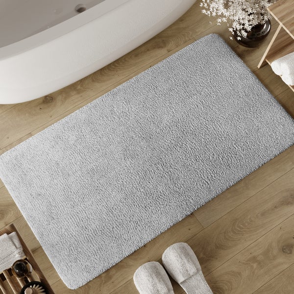 Graue Badematte auf Holzboden neben einer Badewanne in einem hellen, organisierten Badezimmer.