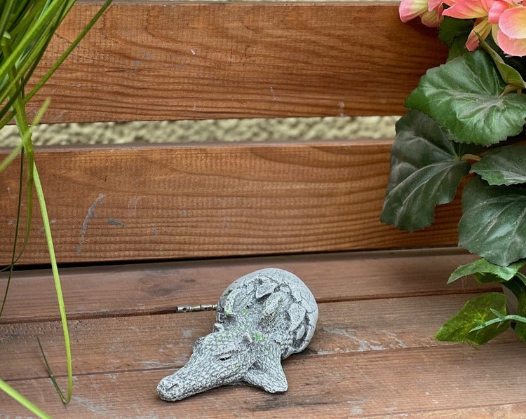 Gartendeko-Figur Krokodil aus Steinguss auf einer Holzbank platziert.