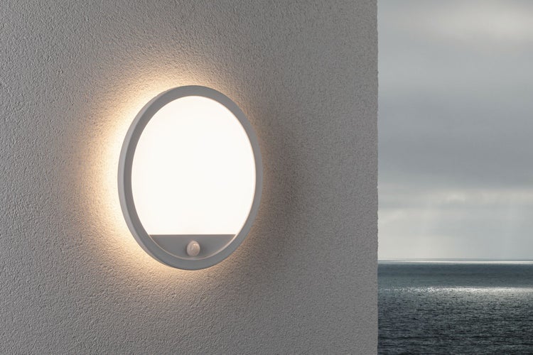 Runde LED Außenwandleuchte mit Bewegungsmelder montiert an einer Hauswand vor einer Meereslandschaft