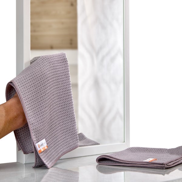 Ein Spiegel wird mit einem Mikrofasertuch gereinigt, ein weiteres Tuch liegt auf der Oberfläche.