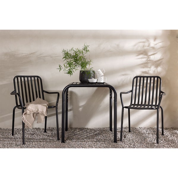 Gartenszene mit zwei schwarzen Metallstühlen und einem quadratischen Tisch mit Topfpflanze