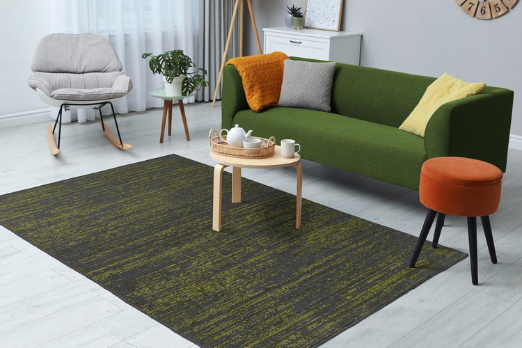 Modernes Wohnzimmer mit dunkelgrau und grün gemustertem Teppich auf hellem Boden, grünem Sofa und Couchtisch aus Holz.