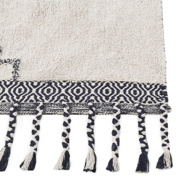 Nahaufnahme eines Hochflor-Badeteppichs mit geometrischer Bordüre und geflochtenen Quasten.