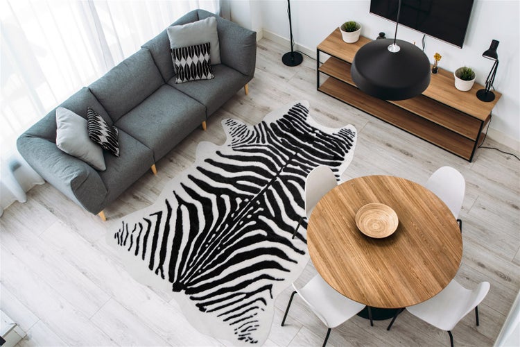 Moderner heller Wohnbereich mit einem Teppich in Zebra-Optik, einem Sofa, einem runden Esstisch aus Holz und einem Sideboard auf einem Holzfußboden.