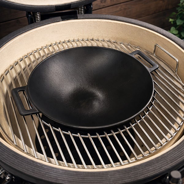 Schwarzer Wok aus Gusseisen auf einem Grillrost in einem Keramikgrill